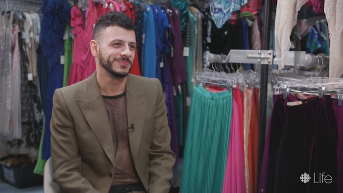 Un homme souriant, dans un magasin rempli de vêtements. 