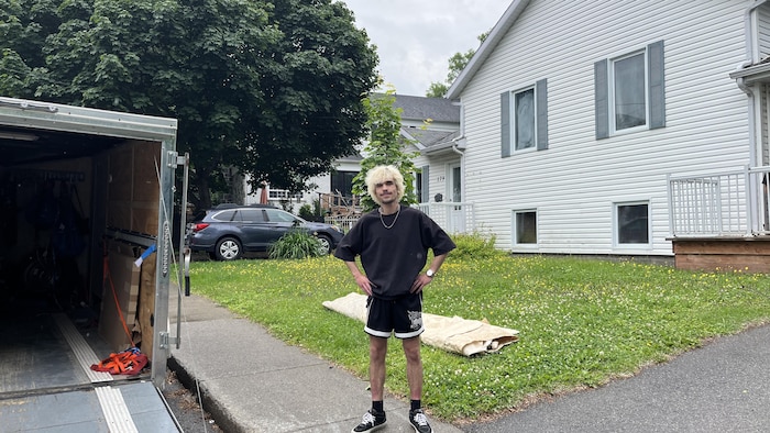 Samuel Boudreau se tient devant son logement et une remorque de déménagement.