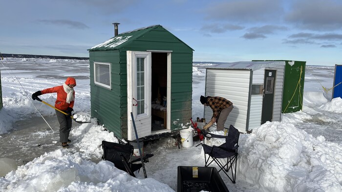 Deux personnes s'activent autour d'une petite cabane munie d'une cheminée.