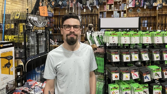 Un homme debout dans un magasin de matériels de pêche regarde la caméra.