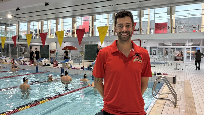 Un homme avec un chandail rouge pose devant une piscine.