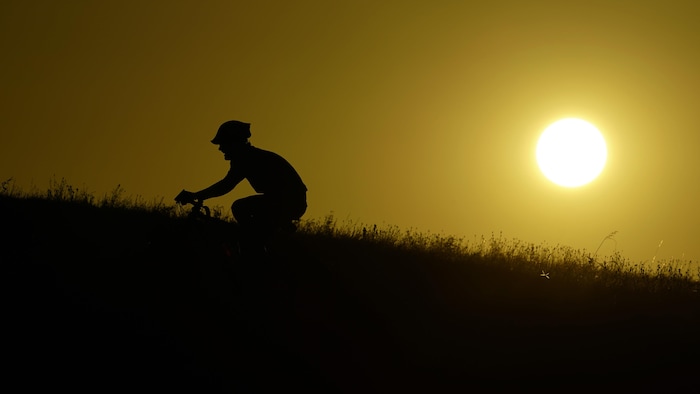 Un cycliste gravit une colline au coucher du soleil.