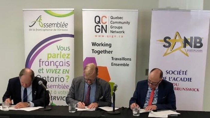 Trois hommes signent un document.