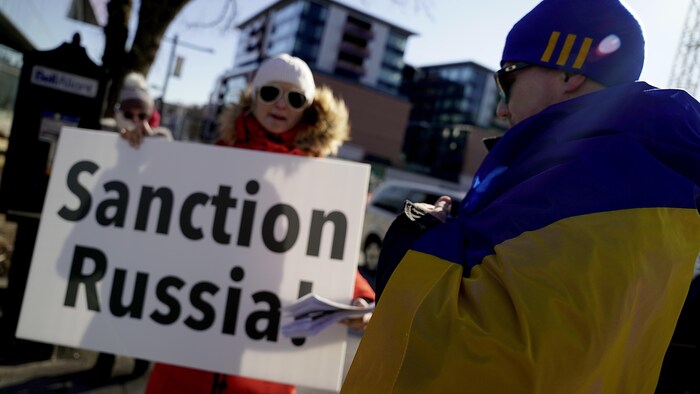 Una mujer en una plaza pública sostiene un cartel con las palabras "Sanción a Rusia".