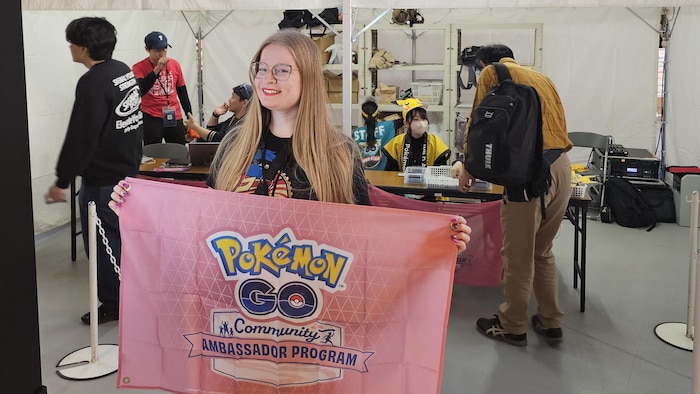 Sandra Maroszek à un événément Pokemon Go, elle tient une bannière du programme des ambassadeurs du jeu, et en arrière-plan il est écrit centre communautaire en anglais et en japonais.