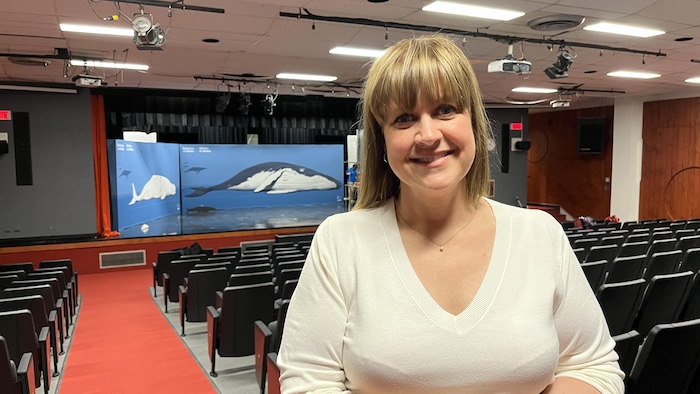 Sandra Gauthier dans un auditorum. Sur la scène de l'auditorium deux immenses images de baleine sont imprimées sur deux toiles. 