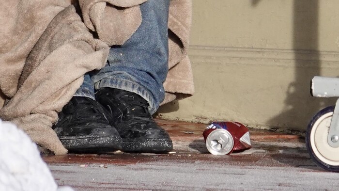 Une personne assise par terre dans la rue, on ne voit que ses pieds.