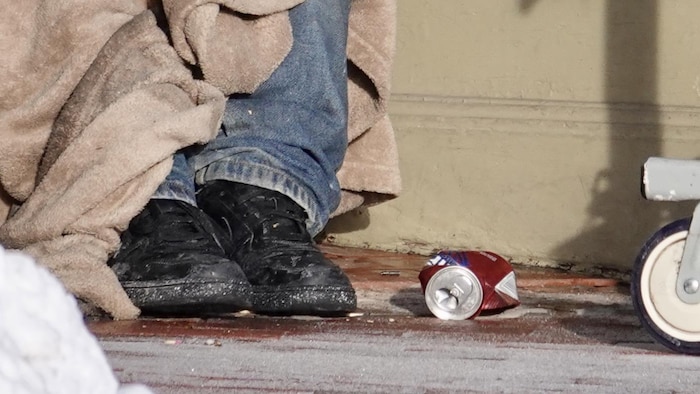 Une personne assise par terre dans la rue, on ne voit que ses pieds.  