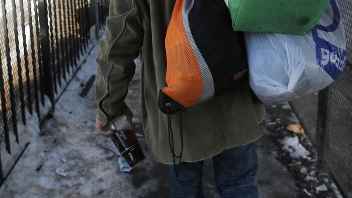 Un homme de dos qui marche dans un couloir extérieur enneigé. Il traîne des sacs sur son dos.