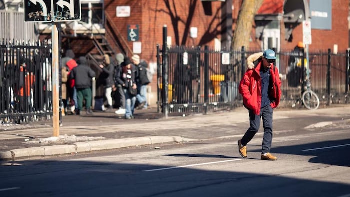 Un homme marche dans la rue. Derrière lui, un groupe de sans-abris.