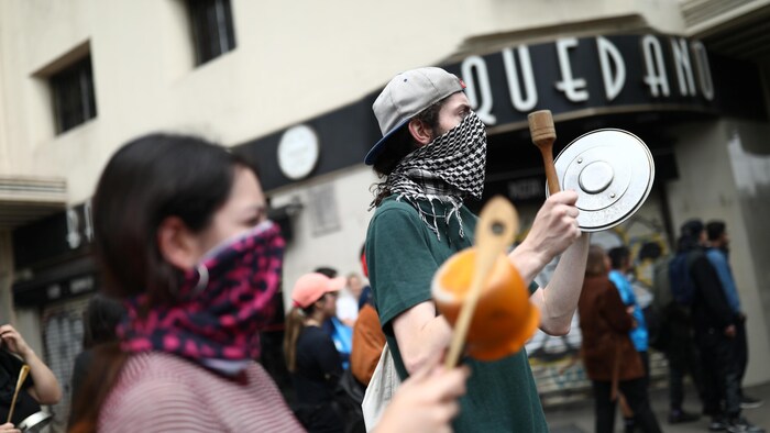 Des manifestants masqués frappent des casseroles dans la rue.