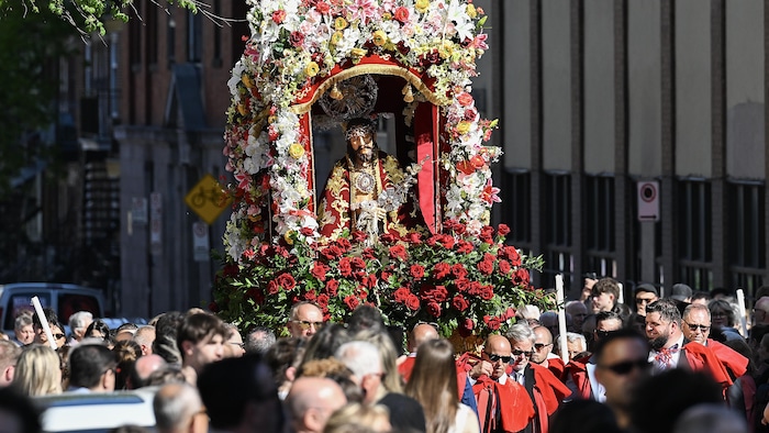 Une statue de Jésus entourée de fleurs est transportée par un groupe de personnes.