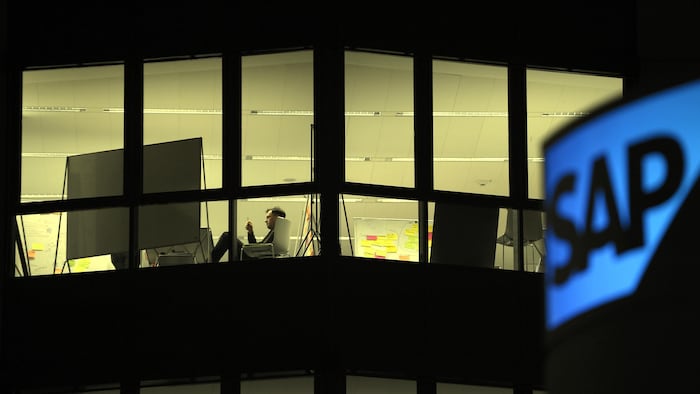Un homme est assis à un bureau devant une fenêtre et le logo de la compagnie S A P.