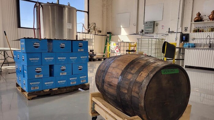 Intérieur d'une distillerie, avec gros baril de bois et caisses empilées. 