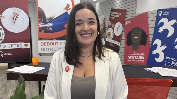Sara Germain sourit à la caméra devant des affiches de Québec solidaire.