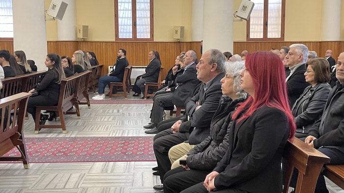 Une femme à la chevelure rouge est assise sur un banc dans une église bondée de monde.