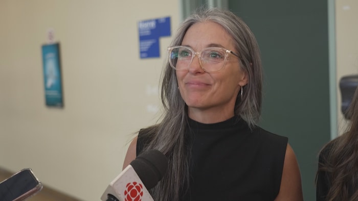 La femme souriante, témoigne devant la caméra et un micro de Radio-Canada.