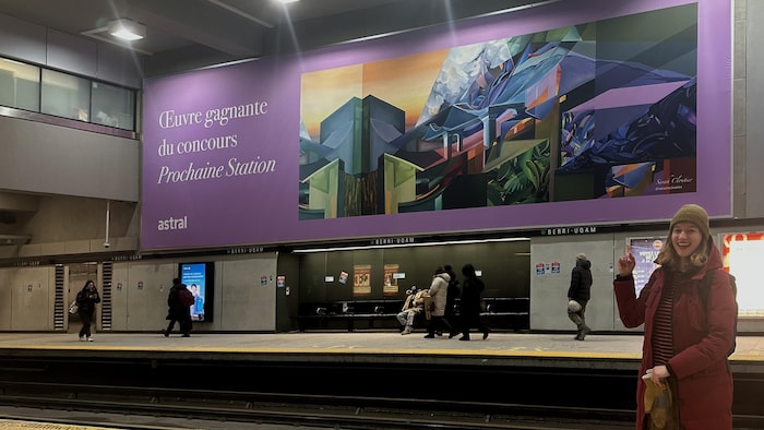 Une jeune femme pointe du doigt une immense oeuvre d'art accrochée dans le métro de Montréal. 