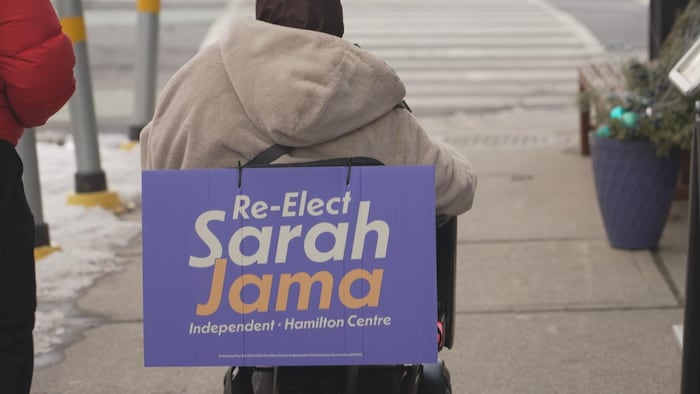Une femme en fauteuil roulant avec une affiche au dos.