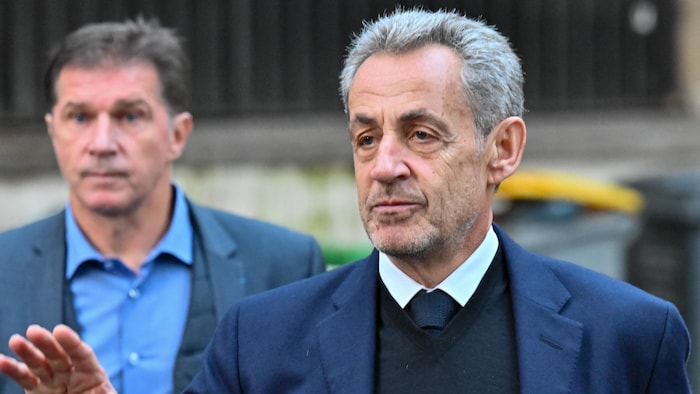 Nicolas Sarkozy quitte son domicile en levant la main droite.