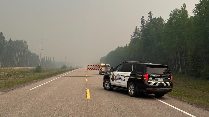 Une voiture du Saskatchewan Marshals Service qui bloque une route en raison d'un feu de forêt.