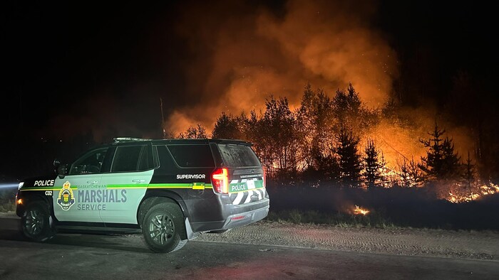 Une voiture du Saskatchewan Marshals Service près d'un feu de forêt, en juin 2025.