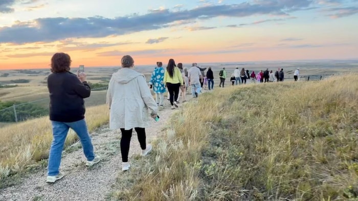 Des visiteurs marchant en file indienne en direction de la falaise des pétroglyphes de Saint-Victor lors d'une visite guidée.
