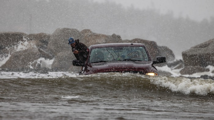 Un homme sort d'une camionnette immobilisée sur une route inondée. 