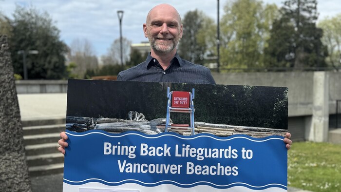 Un homme tenant une pancarte qui demande le retour des sauveteurs sur des plages de Vancouver. 