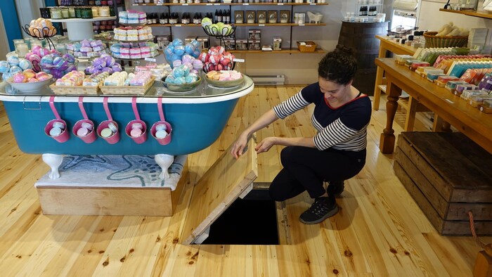 Une femme ouvre une trappe au niveau du plancher dans un boutique de savon.