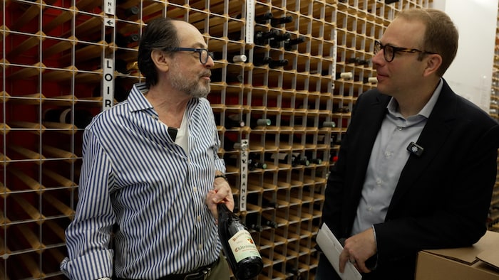 Un homme présente une bouteille de vin à un journaliste.