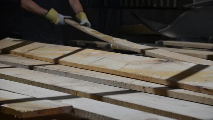 Un ouvrier manipule des planches dans une scierie.