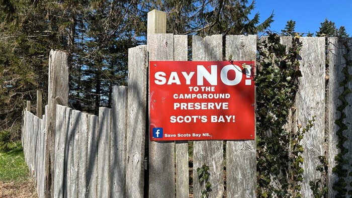 Une pancarte rouge « Dites non au terrain de camping » est clouée à une clôture de bois.