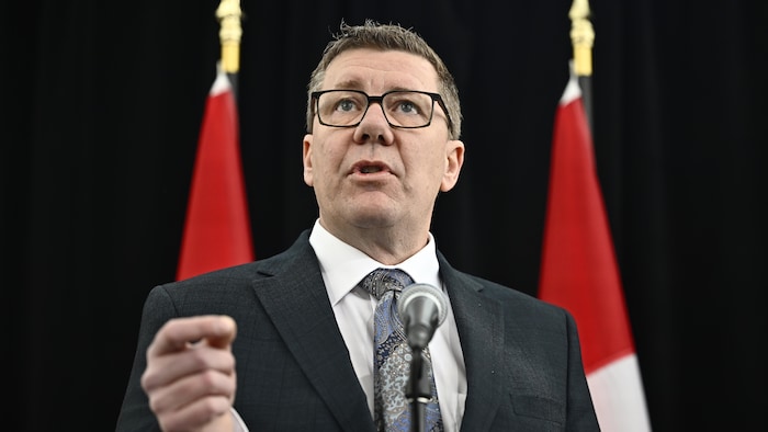 Le premier ministre de la Saskatchewan, Scott Moe, devant les drapeaux canadiens.