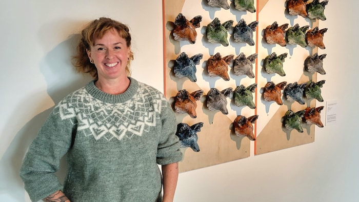 Claire-Alexie Turcot pose près de son œuvre, constituée de petites têtes de renard.