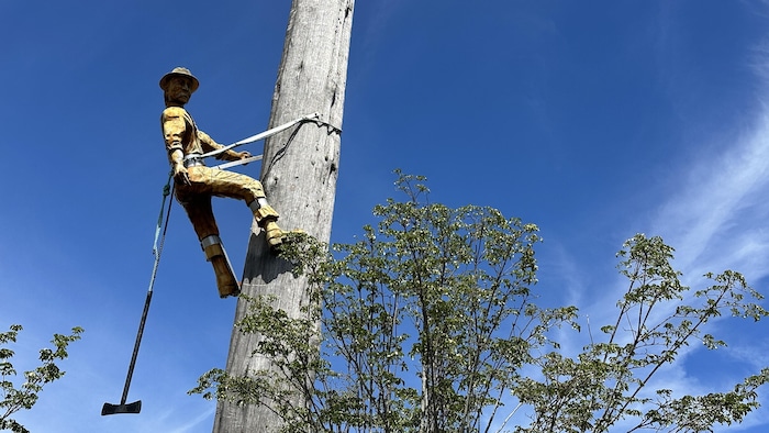 Une sculpture d'un travailleur forestier accroché à un poteau en bois.