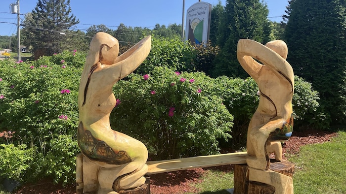 Une œuvre commémorative en bois représentant deux personnages qui ont les mains jointes à Rivière-Éternité.