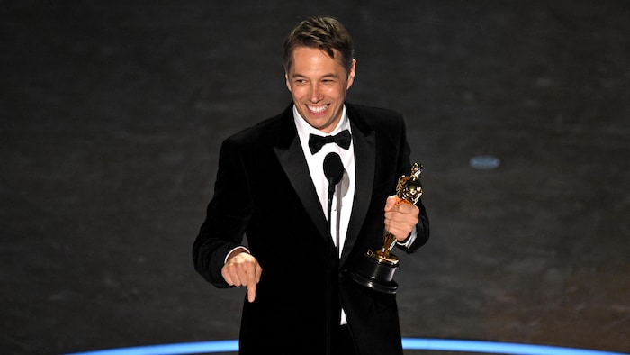 Sean Baker tient un trophée devant un micro sur scène.