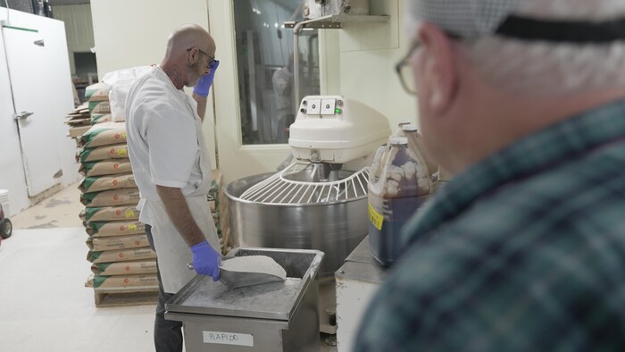 Sean Boucher met les ingrédients du pain dans un mélangeur, sous le regard de Simon. 