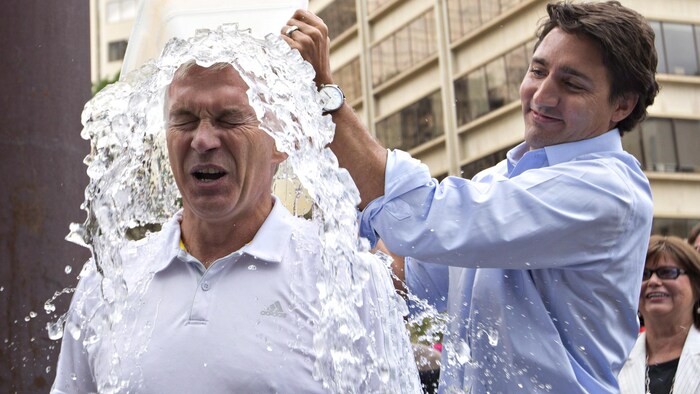 Sean Casey plisse les yeux pendant que de l'eau et de la glace s'abattent sur sa tête, sortie du bac en plastique que Justin Trudeau tient au-dessus de sa tête, en affichant un sourire narquois.