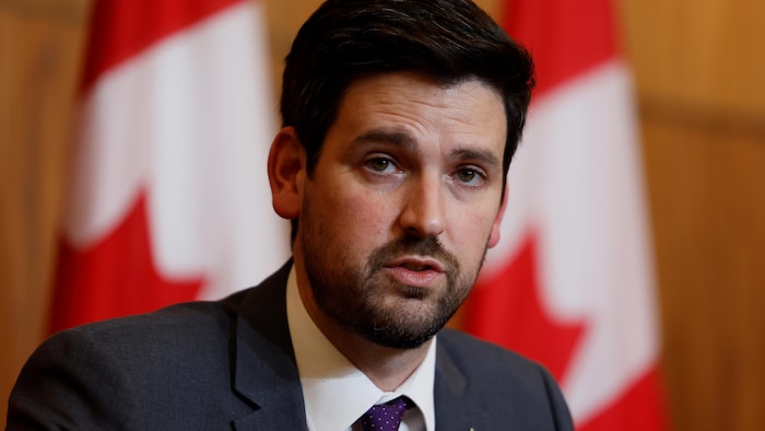 وزير الهجرة واللاجئين والمواطنة الكندي، شون فرايزر، يتحدث في مؤتمر صحفي وخلفه أعلام كندية.