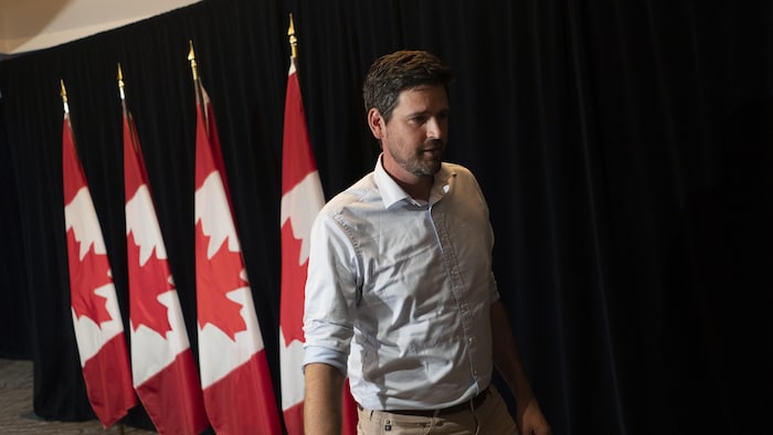 Sean Fraser marche devant des drapeaux du Canada dans une salle de presse.