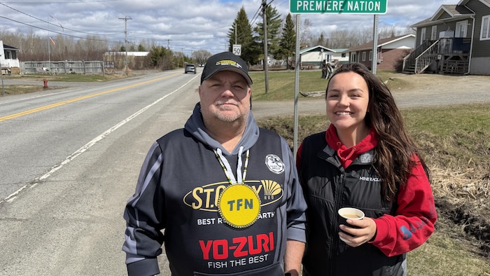 Sean McLaren et sa fille prennent la pose au bord de la route, devant le panneau d'entrée de la communauté.
