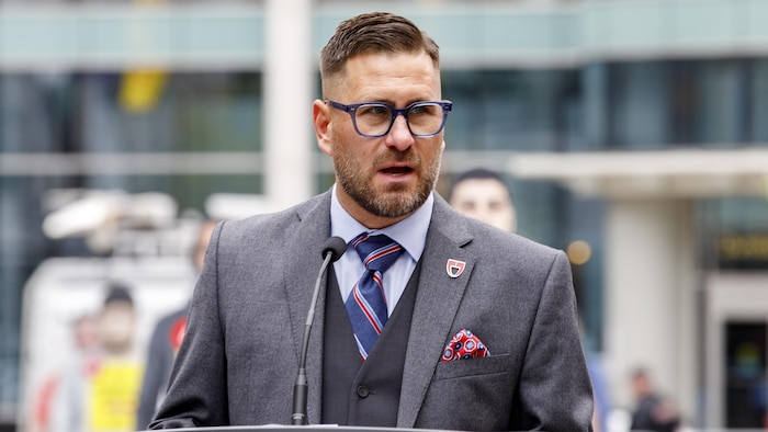 L'homme porte un complet et parle à un podium lors d'un point de presse.