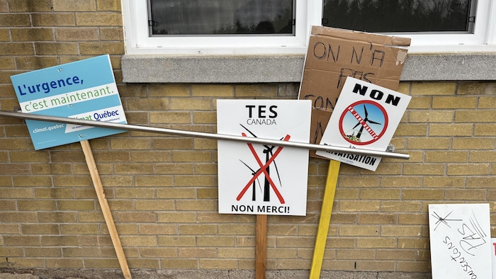 Des pancartes d'opposants à TES Canada appuyées conte un mur.