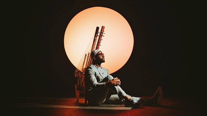 L'artiste pose devant sa kora, un instrument à cordes, assis devant un cercle jaune. 