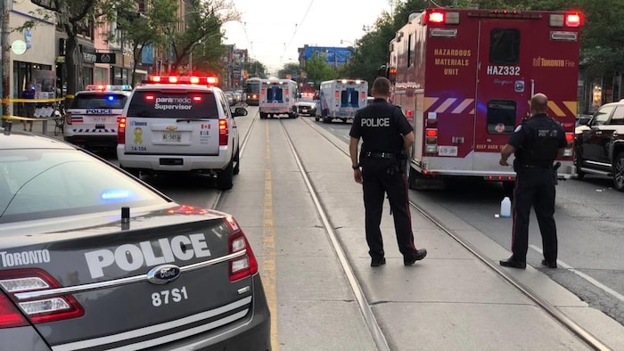 Des autopatrouilles de police, deux ambulances et un camion de pompier bloquent une rue.
