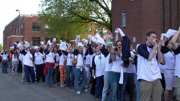 Des jeunes font la file en agitant des mouchoirs.