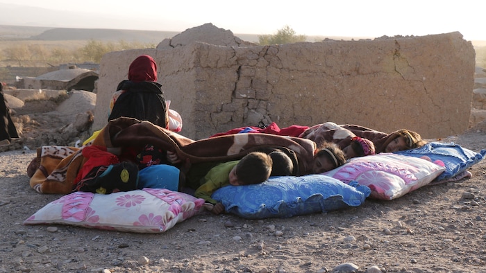 Afghan children rest under a blanket next to damaged homes after the earthquake that struck Sarbuland village in Zandiya district.