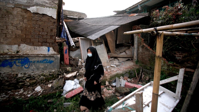 Une femme marche devant des maisons détruites par le séisme.
